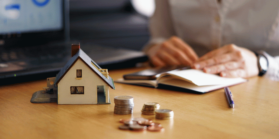 Maison miniature et pièces de monnaies posées sur un bureau (c) Freepik